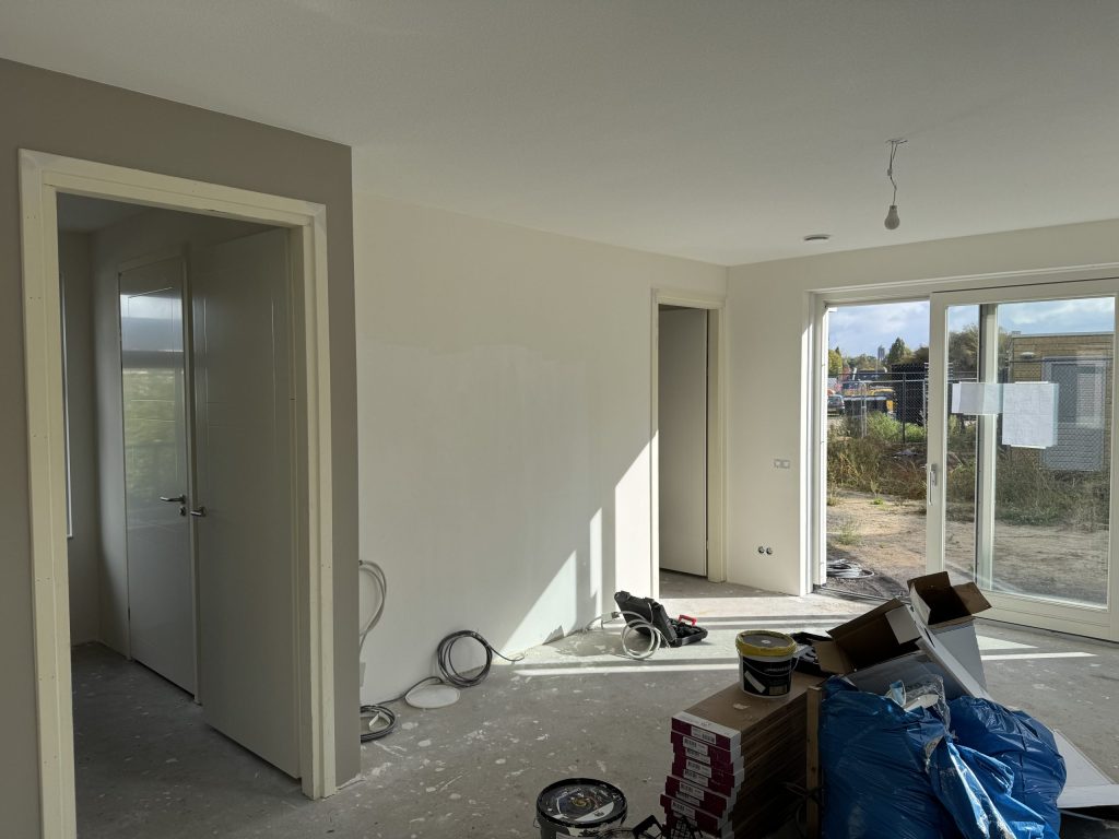 Net opgeleverde woonkamer met kale betonvloer en dozen laminaat