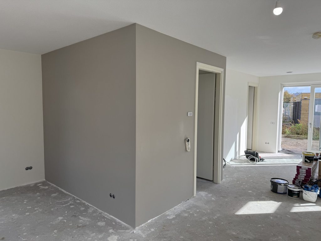 Nieuwbouwwoning met een pas gesausde grijze wand, een betonvloer en verfemmers bij de tuindeur