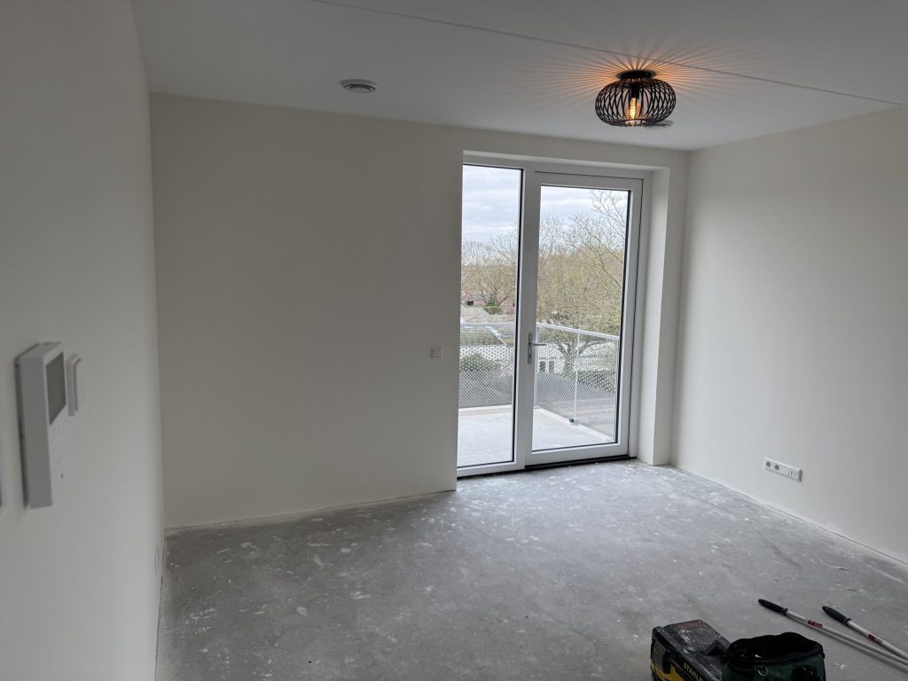 Lege kamer in een nieuw appartement met witte wanden en een balkondeur vlak na de oplevering