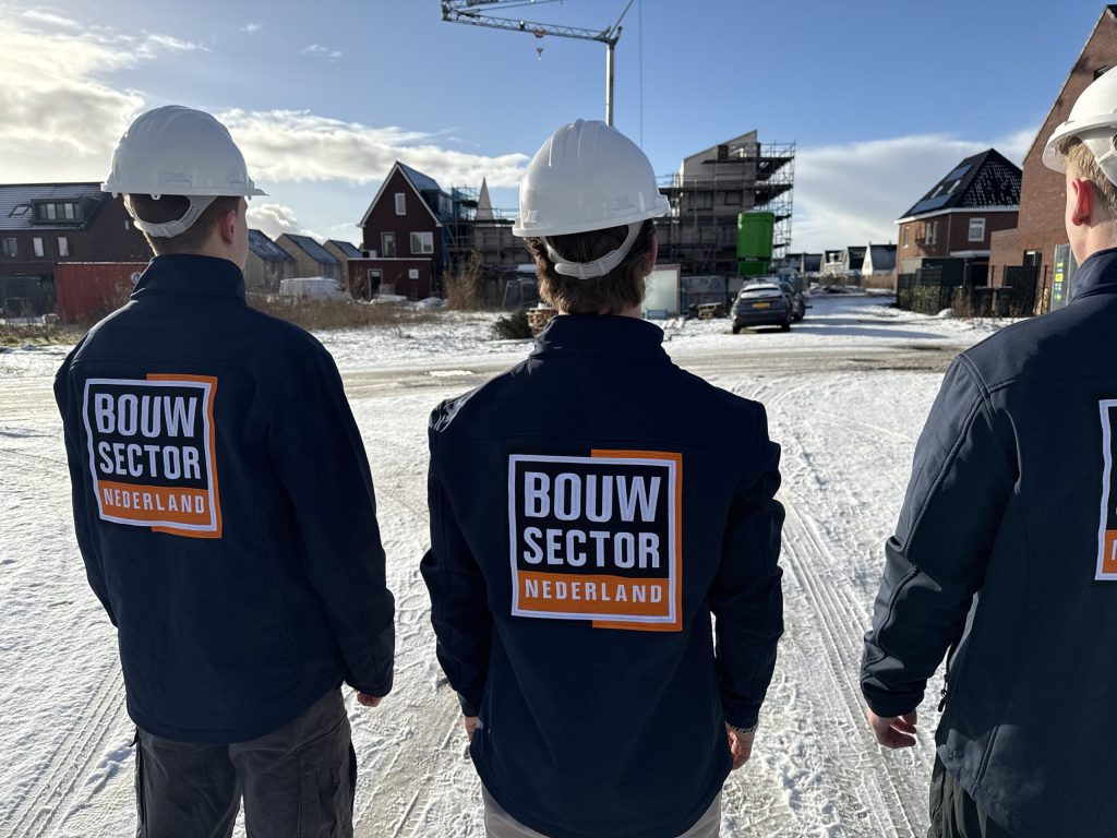 Drie vakmensen in donkere jassen met helm kijken naar huizen in aanbouw in een besneeuwde straat